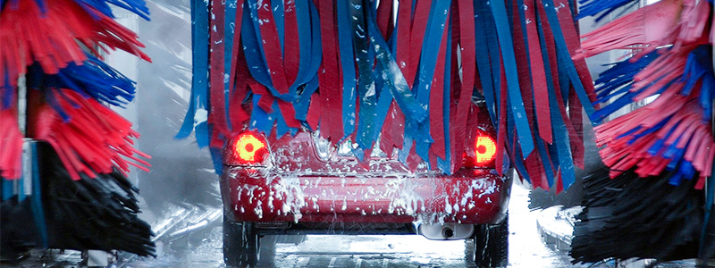 Röd bil som åker genom en biltvätt. 